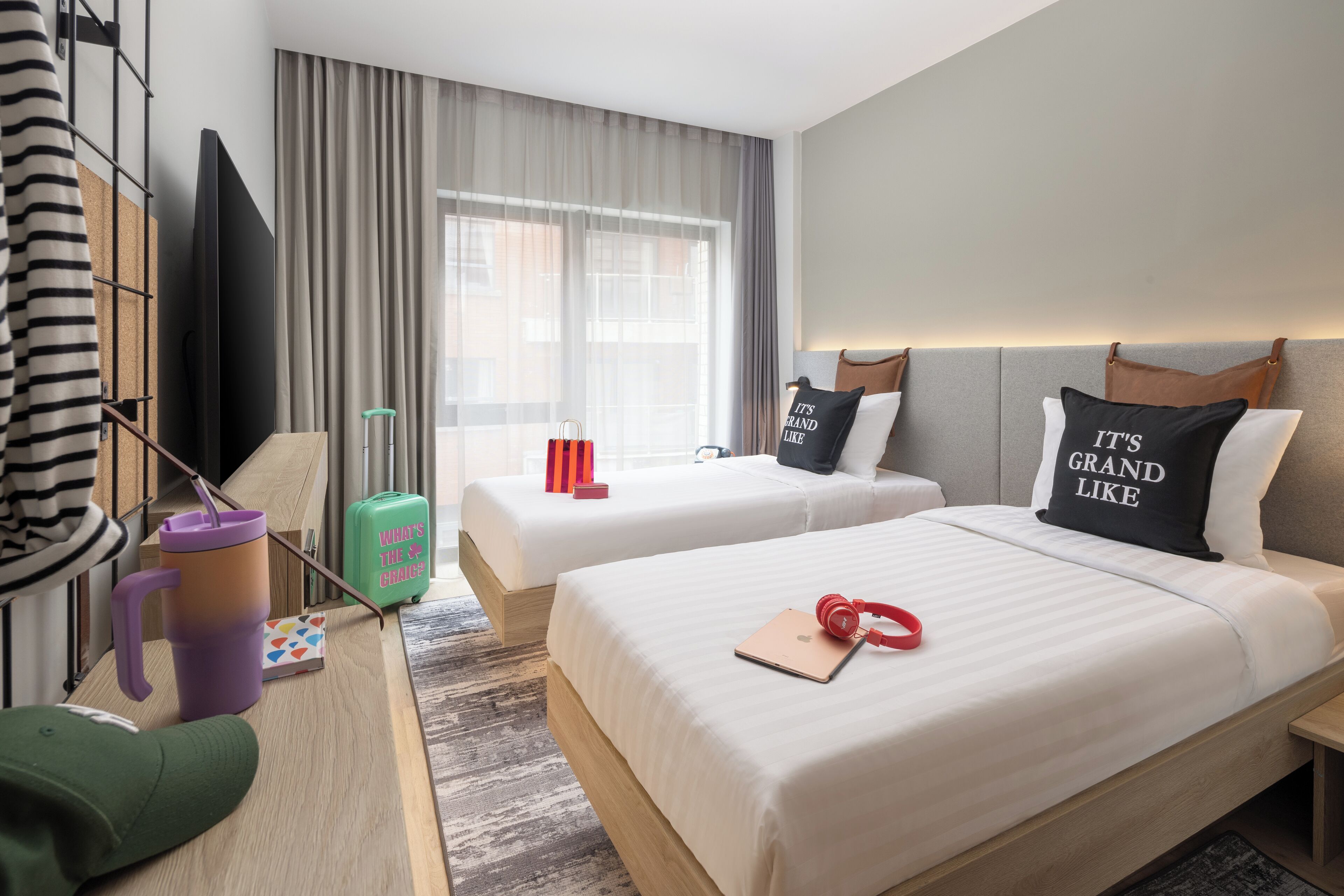 Een hotelkamer met twee bedden, een bureau, een televisie en een raam met gordijnen.