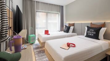 A hotel room with two beds, a desk, a television, and a window with curtains.