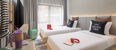 A hotel room with two beds, a desk, a television, and a window with curtains.