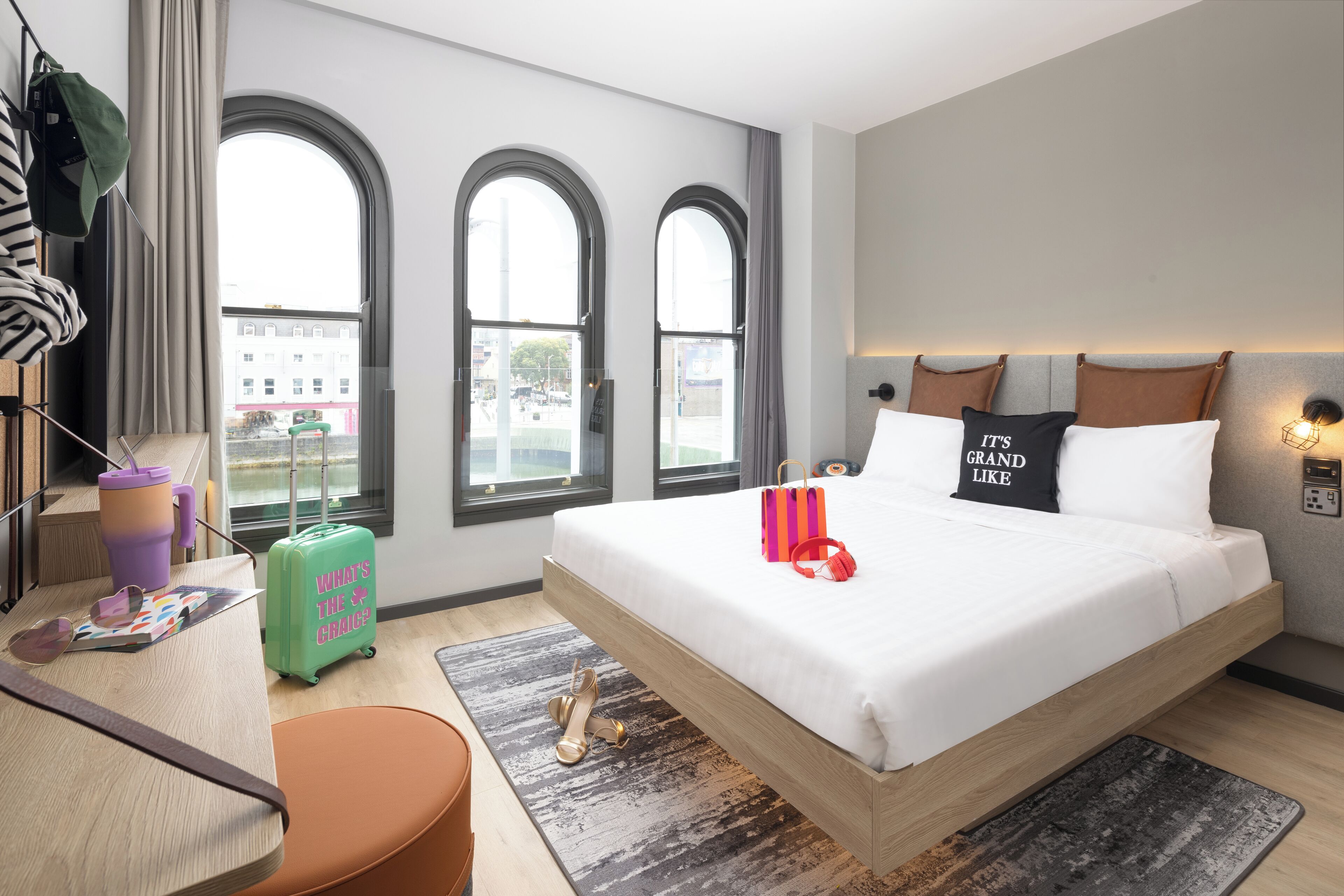 Habitación de hotel moderna con una cama grande, un escritorio y vistas de la ciudad a través de ventanales de arco.