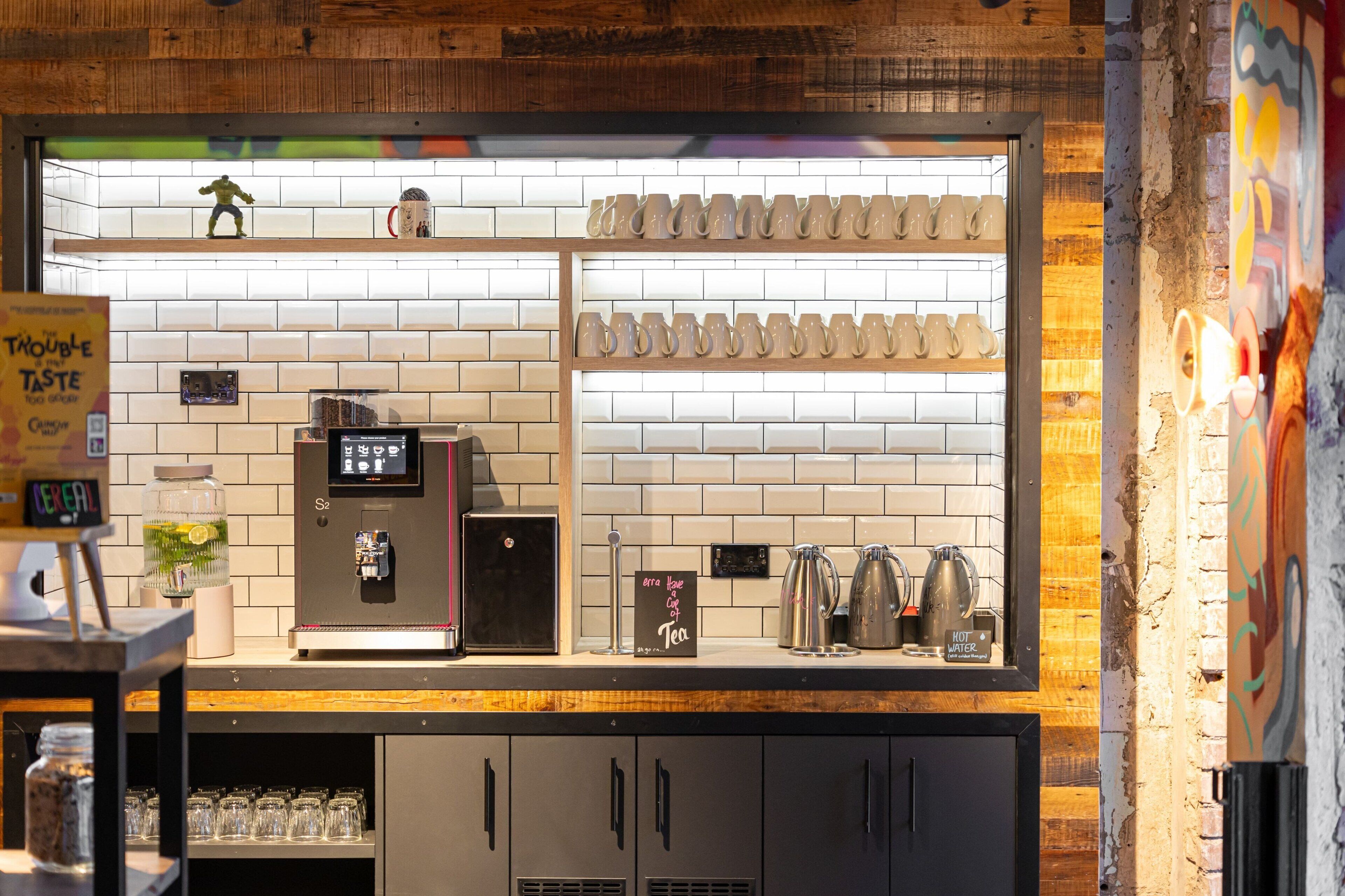 Mostrador de cafetería con una máquina de café, tetera y una exhibición de tazas.