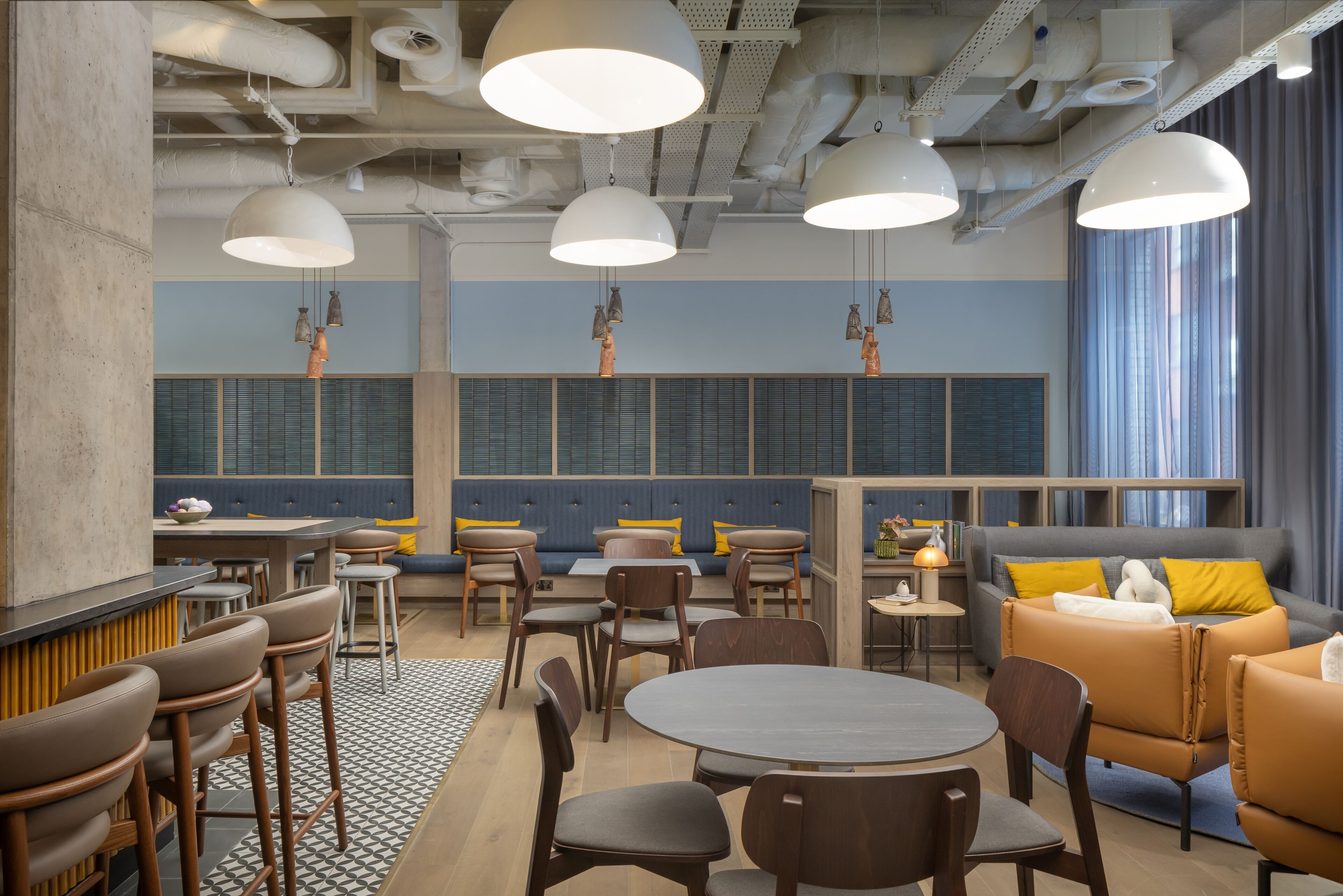 Un restaurante moderno con techos altos, conductos expuestos e iluminación colgante. Hay varias zonas de estar, incluyendo un bar, cabinas y un sofá.