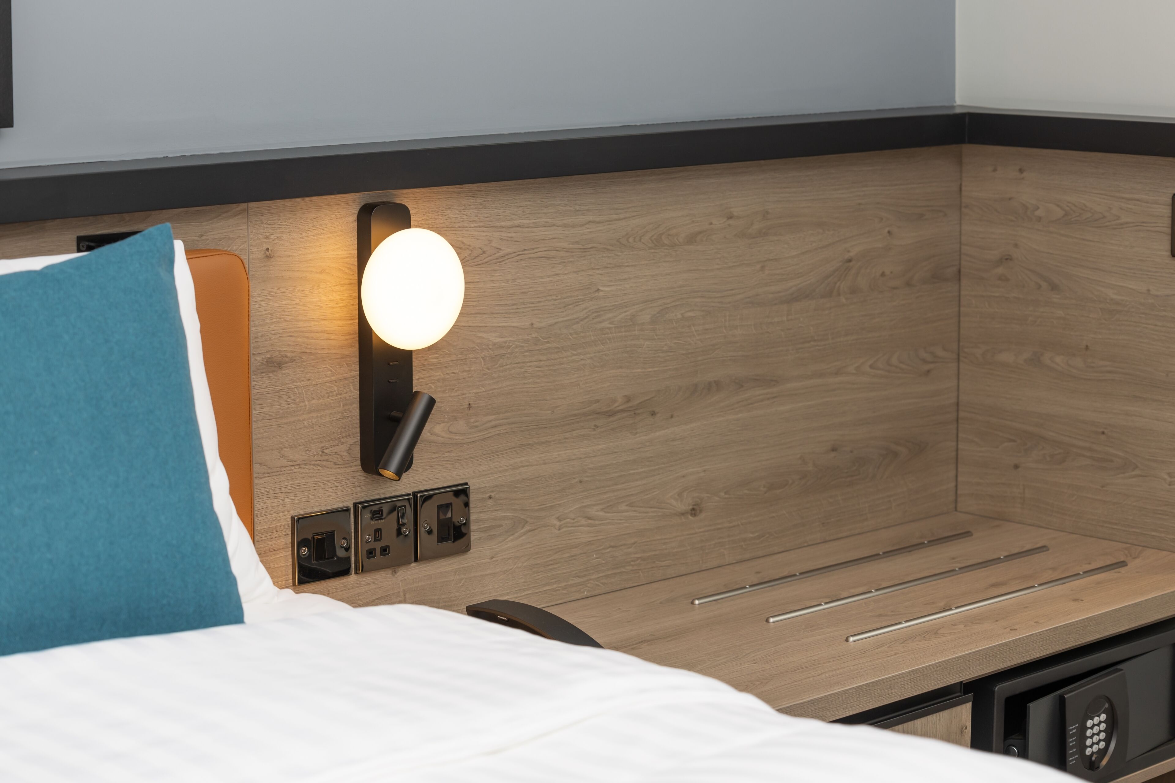 Habitación de hotel con cama, luz empotrada, enchufes y panel de control.