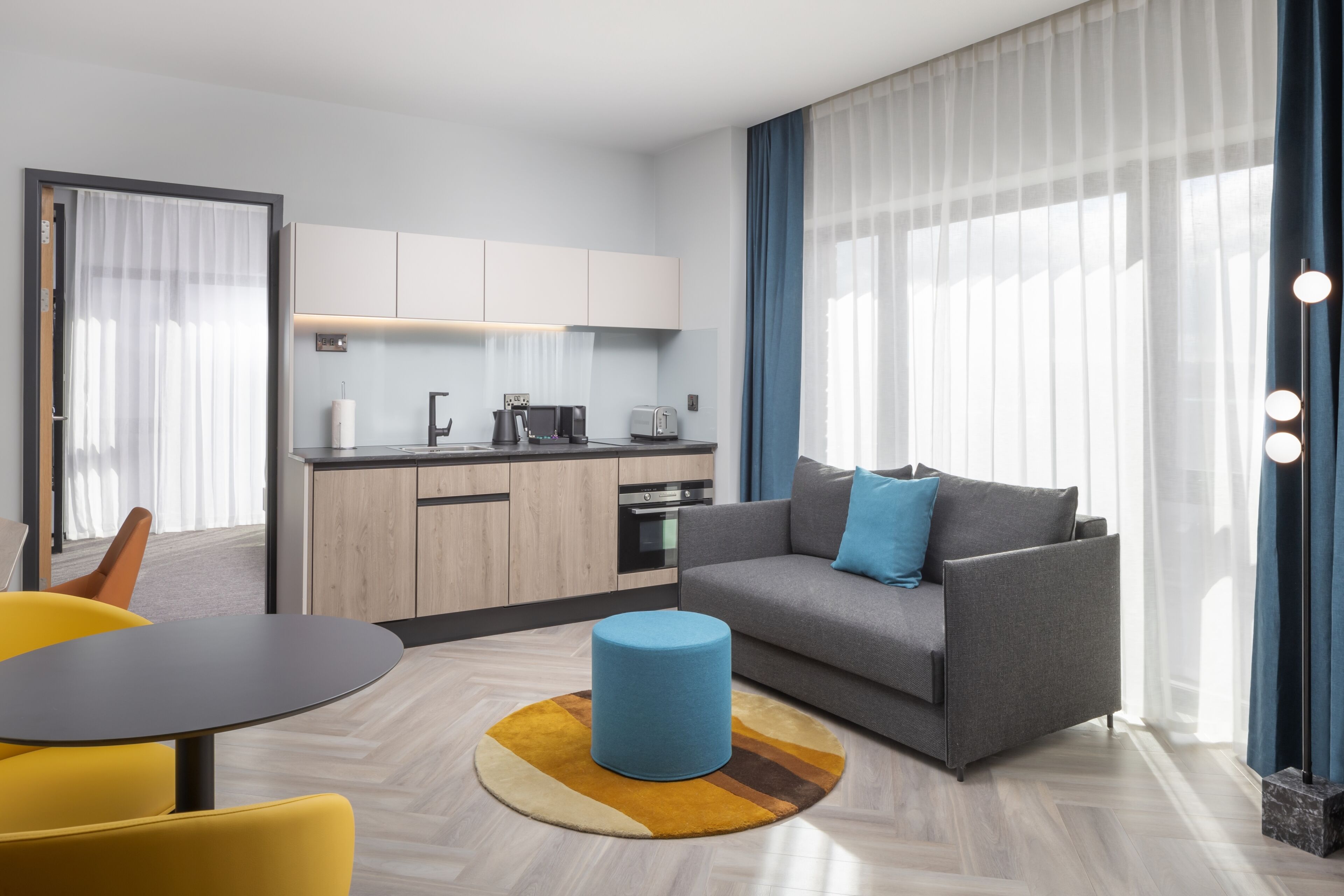 A modern living room with a sofa, a round coffee table, a dining table, and a kitchen area with cabinets and appliances.