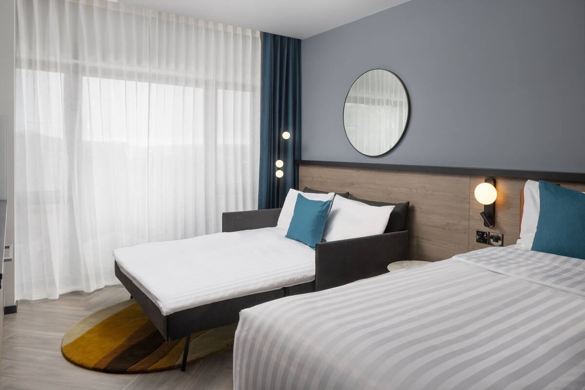 Ein Hotelzimmer mit zwei Betten, einem runden Spiegel und einem Nachttisch mit Lampe.