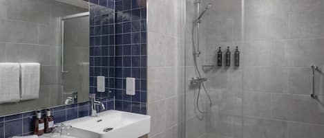 Ein modernes Badezimmer mit einer in Glas eingefassten Dusche, einem weißen Waschbecken und einem Spiegel darüber.