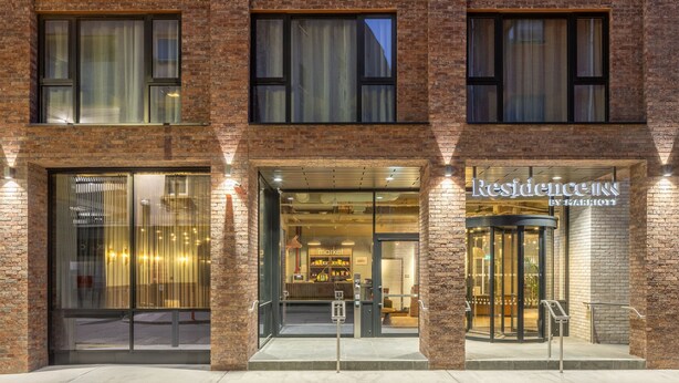 Un bâtiment en briques doté de grandes fenêtres et d’une entrée en verre. L’enseigne indique : « Residence Inn by Hilton ».