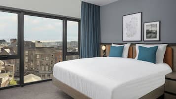 Una habitación de hotel con una cama grande, vista a la ciudad, una mesita de noche y dos cuadros en la pared.