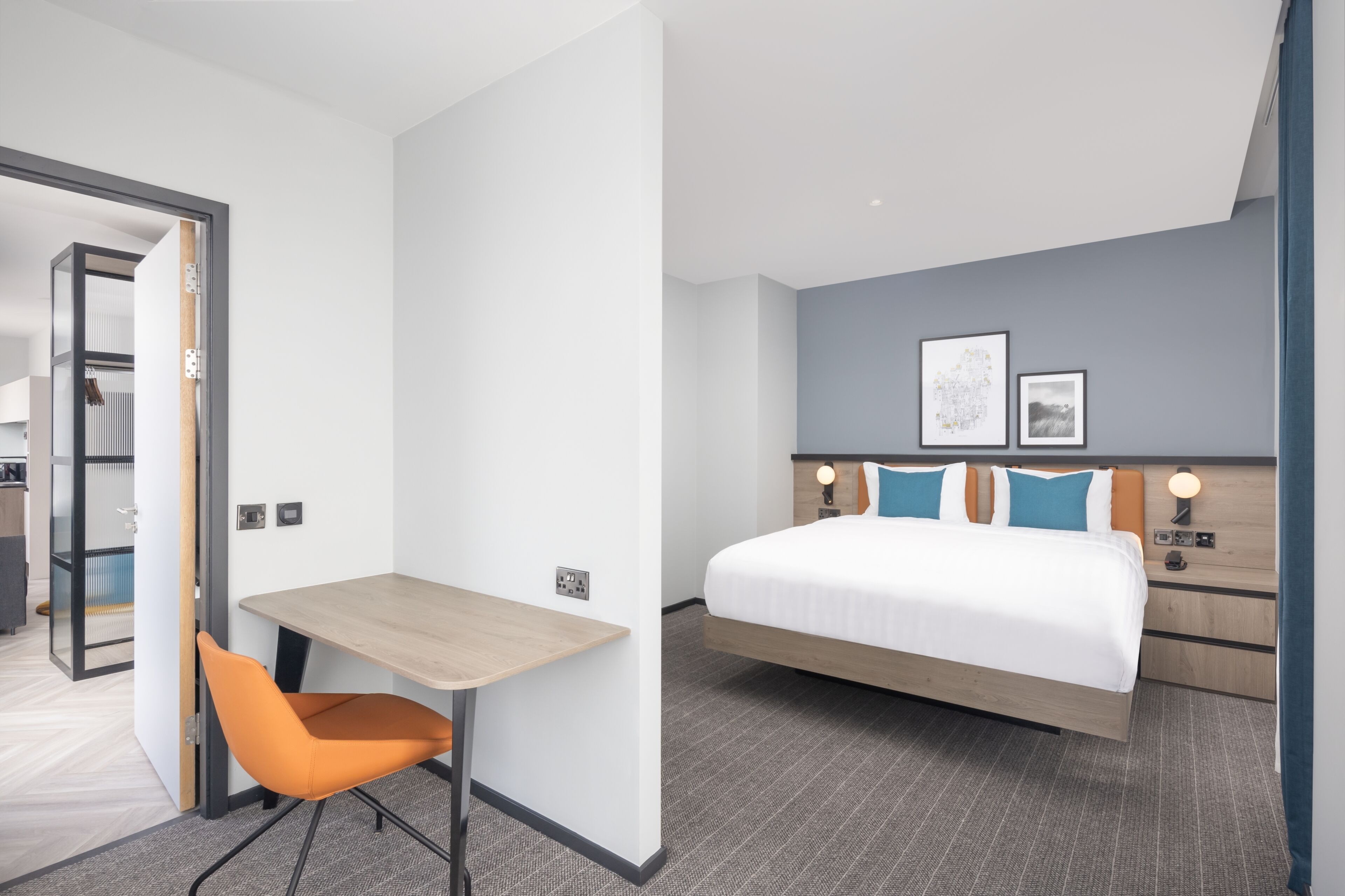 A modern hotel room with a bed, bedside tables, a desk, and a chair.