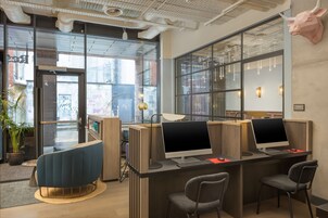 A modern workspace with three desks, each with a computer and a lamp. There are two chairs and a potted plant.