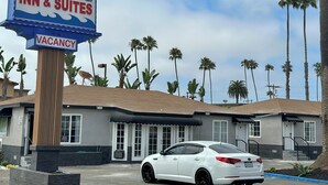 A Oceanside Inn & Suites sign with a vacancy notice, a white car parked in front, and palm trees in the background. - Oceanside Inn & Suites (Oceanside)