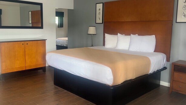 A hotel room with a large bed, a wooden headboard, a wardrobe, and a mirror on the wall. - Oceanside Inn & Suites (Oceanside)