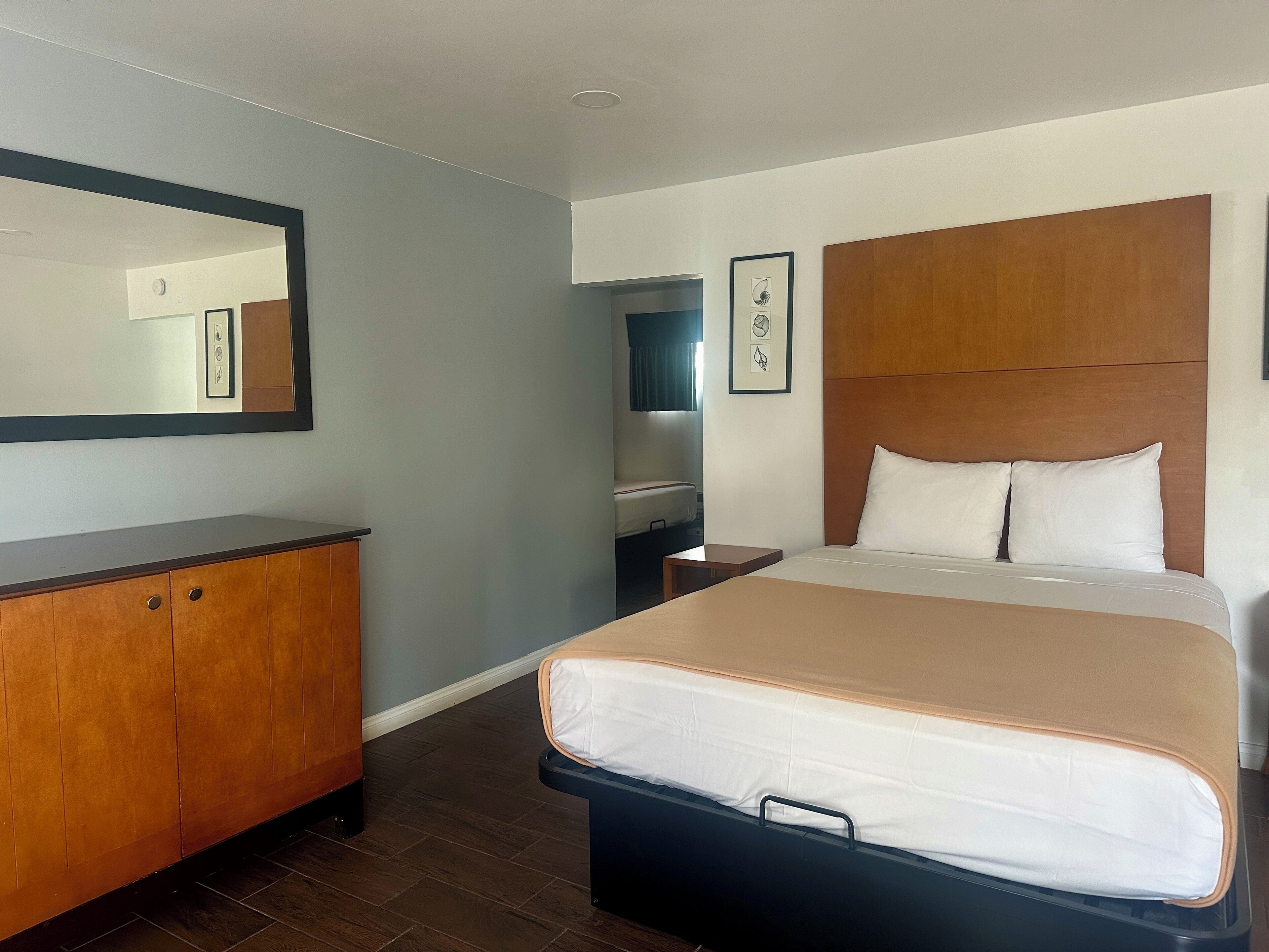 Een hotelkamer met een groot bed, een houten dressoir, een spiegel en een lijst met een afbeelding aan de muur.