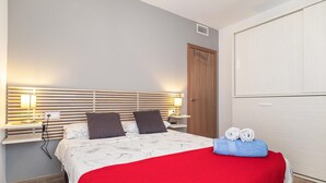 Hotellihuone, jossa on sänky, kaksi yöpöytävalaisinta, puinen sängynpääty, vaatekaappi ja punainen peitto.