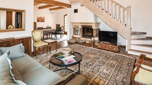 A spacious living room with a sofa, a coffee table, a fireplace, a television, and a staircase.