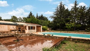 A backyard with a swimming pool, a wooden deck, and a stone wall.