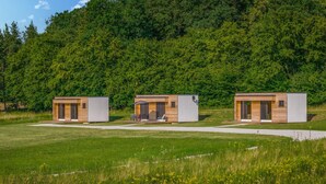 Tres cabañas modernas con amplios ventanales, un patio y un bosque de fondo.