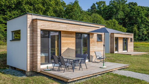 Una cabaña de madera moderna, de un solo nivel, con un patio que incluye una mesa y sillas.