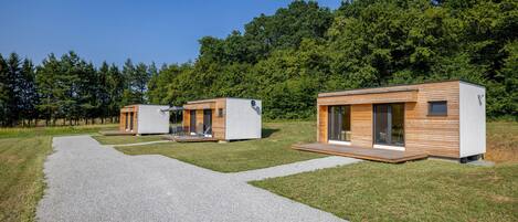 Ein modernes Holzhaus im Freien mit einem Kiesweg, umgeben von einem Wald.