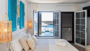 Une chambre à coucher avec un lit, des oreillers, une lampe de chevet et une vue sur les bateaux et l’eau, visible à travers une porte ouverte.