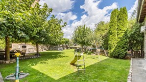A backyard with a grassy lawn, a yellow slide, a swing set, and a stone wall. - Apartment 'Cambolino' with Mountain View, Private Terrace and Wi-Fi (Borrastre)
