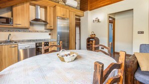 Una cocina con armarios de madera, un refrigerador de acero inoxidable y un microondas. Hay una mesa de comedor con una cesta y una silla.