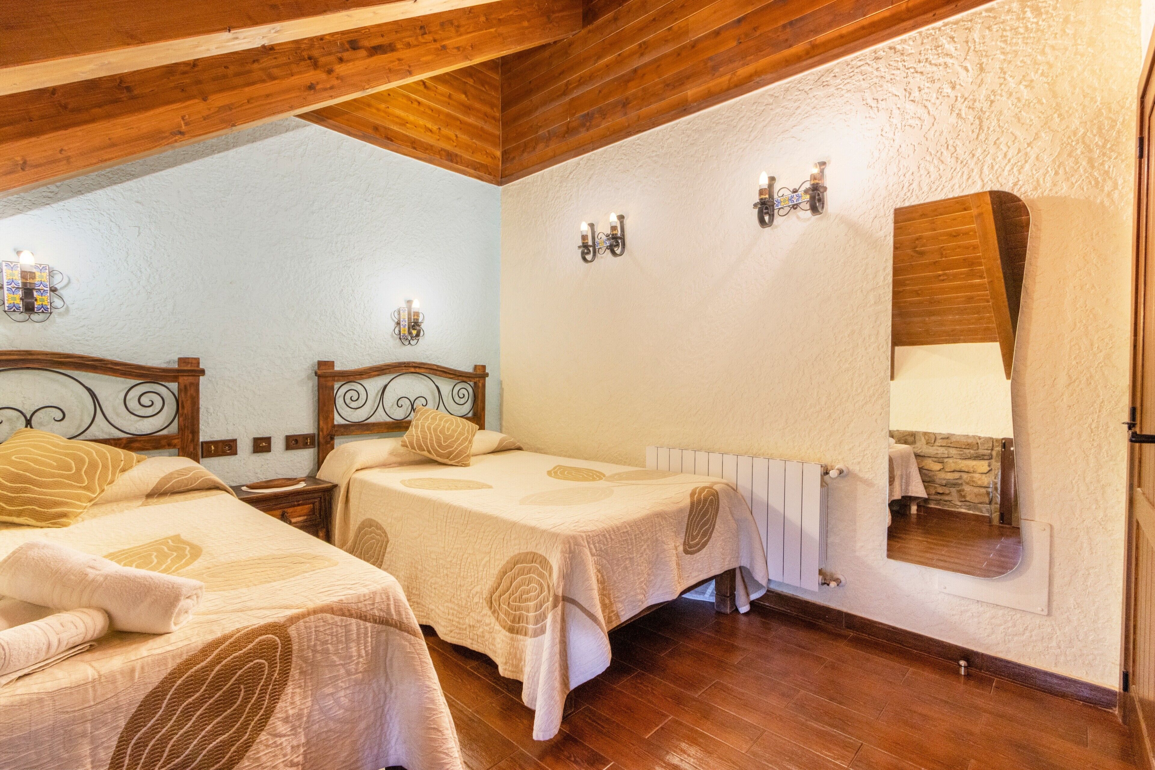 Una habitación con dos camas, vigas de madera, una pared de piedra y un espejo.