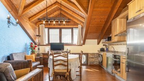 Un interior de madera con una mesa de comedor, sillas, un sofá, un televisor y electrodomésticos de cocina.