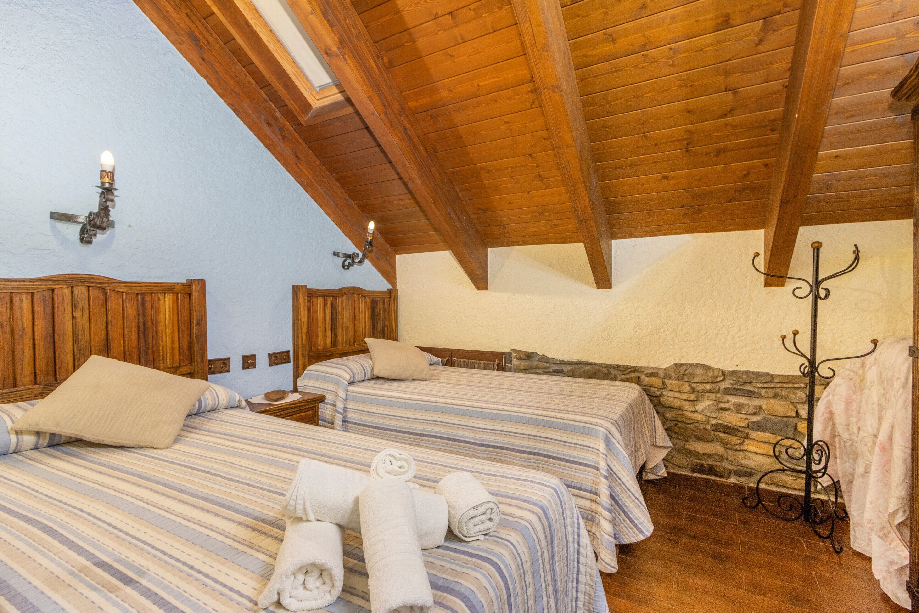 A room with two beds, wooden beams, stone wall, and a coat rack.