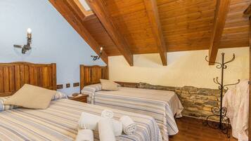 A room with two beds, wooden beams, stone wall, and a coat rack.