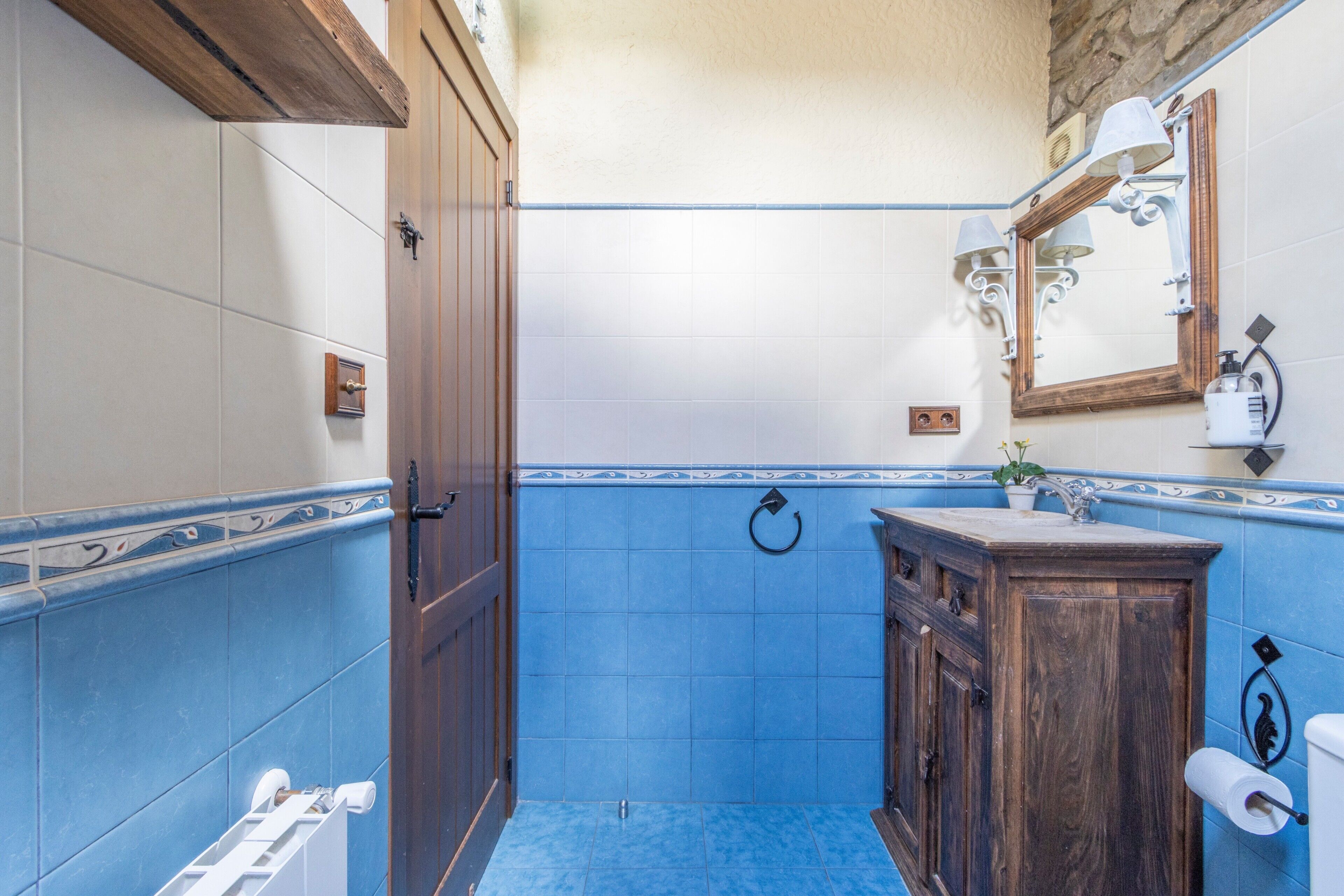 A bathroom with blue tiles, a wooden door, a sink with a mirror, and a towel rack.