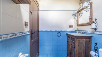 A bathroom with blue tiles, a wooden door, a sink with a mirror, and a towel rack.
