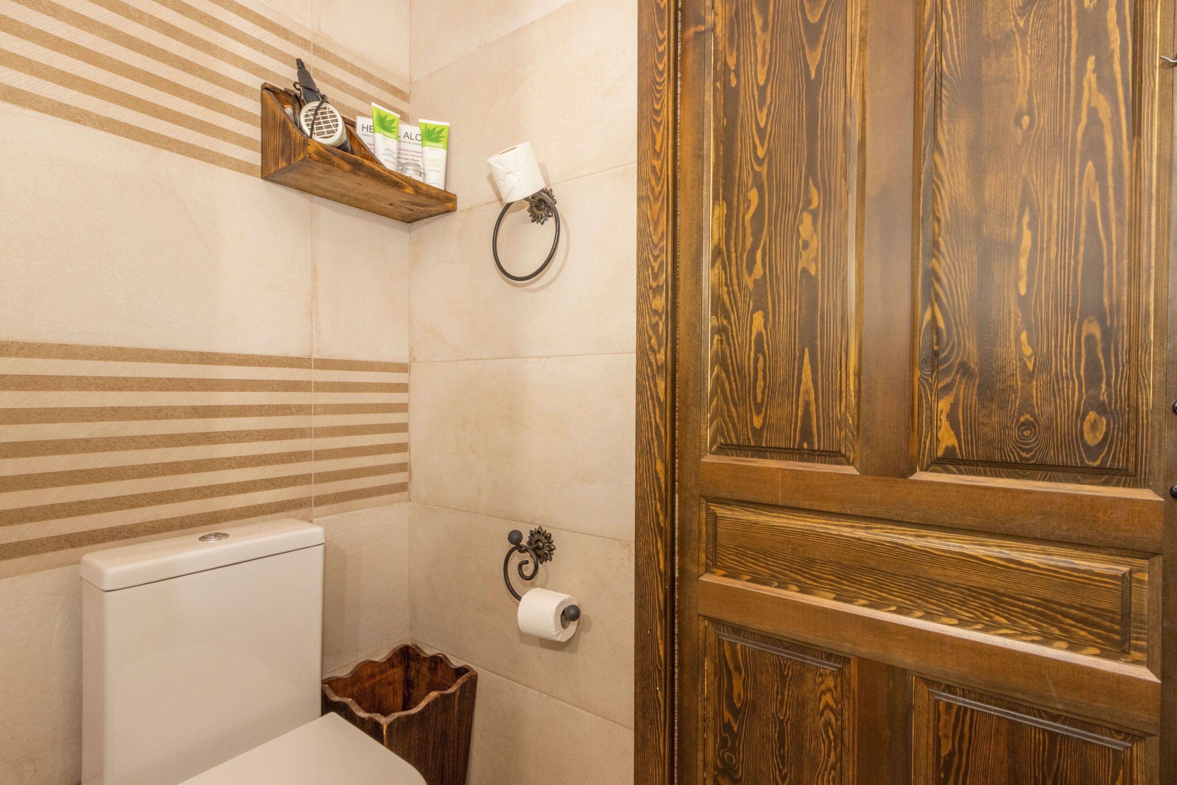 A bathroom with a wooden door, a toilet, a shelf with toiletries, and a towel ring.