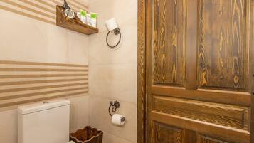 A bathroom with a wooden door, a toilet, a shelf with toiletries, and a towel ring.