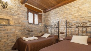 Una habitación con paredes de piedra, dos camas con ropa de cama marrón, techo de madera y una chimenea de piedra.