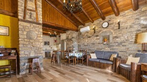 Un interior rústico con paredes de piedra, vigas de madera, una zona de comedor con mesa y sillas, y un sofá.