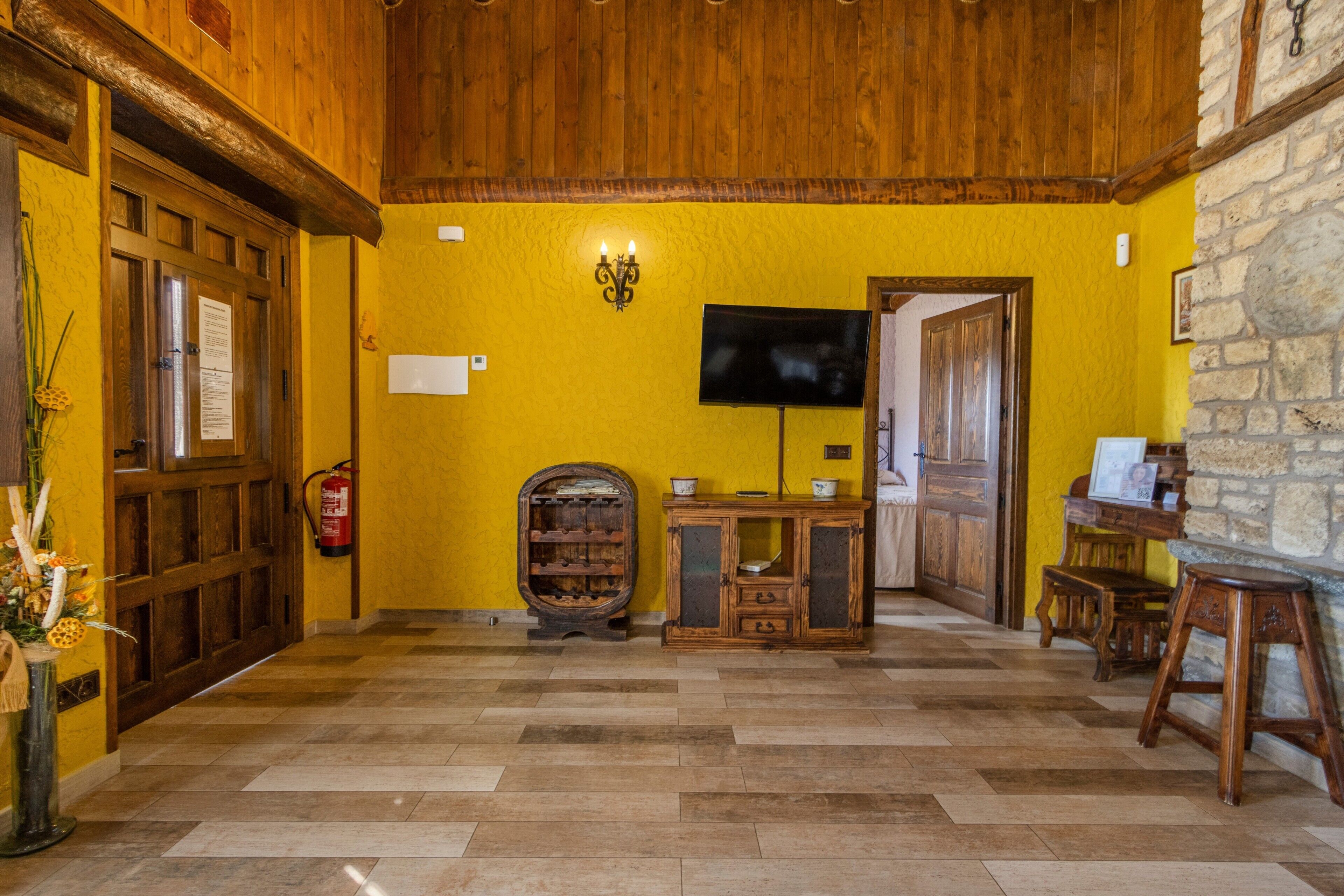 Un hall con suelo de madera, televisión, botellero y pared de piedra.