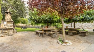 Eine Terrasse im Freien mit Steintischen und -bänken, umgeben von Bäumen und einer Steinmauer.