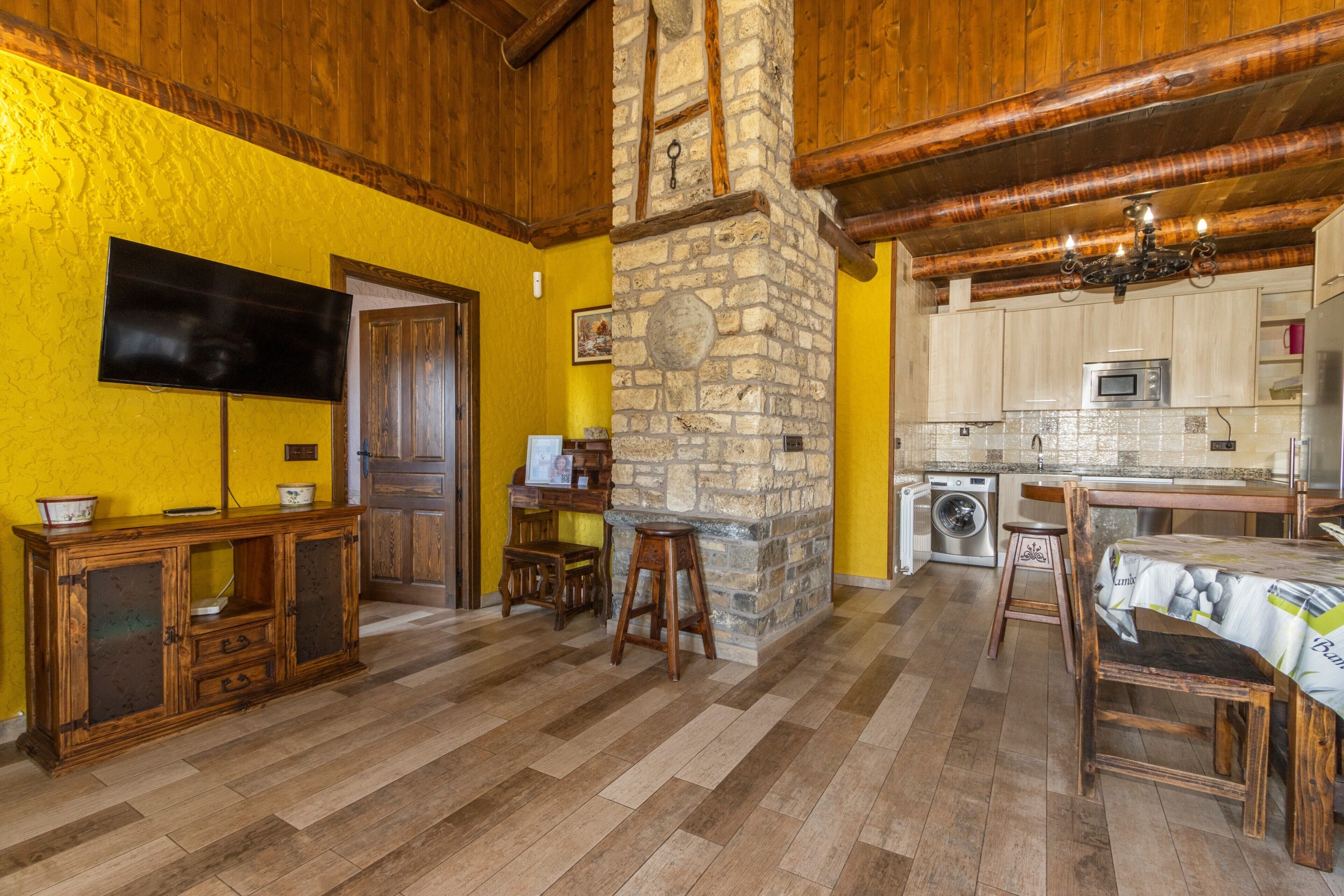 Una cocina con pared de piedra, techo de madera y televisor de pantalla plana montado en la pared.