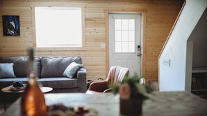 A cozy living room with a grey sofa, a small table with a vase, and a wooden door. - Raven's Spruce Suite #7 Getaway (Fairbanks)
