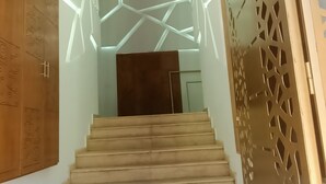 Una escalera con patrones de luz geométricos en las paredes, puertas de madera y un suelo sencillo.