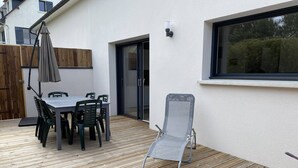 Une terrasse avec une table et des chaises, une chaise pliante et une fenêtre donnant sur un jardin.