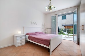 A bedroom with a bed, a nightstand, a dresser, a chandelier, and a sliding glass door leading to an outdoor area.