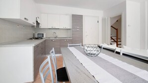 Una cocina moderna con armarios blancos, un comedor con una mesa larga y una escalera que sube a un dormitorio tipo loft.