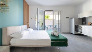 Une chambre d’hôtel moderne avec un lit, un mur d’accent vert, un coin cuisine et un balcon avec des chaises.
