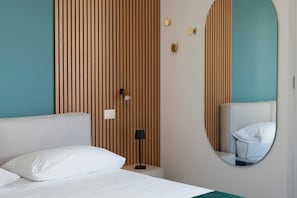 Une chambre d’hôtel comprenant un lit, une table de chevet, une lampe, un miroir fixé au mur et un mur recouvert de panneaux en bois.
