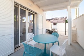 Une terrasse couverte avec une table ronde et des chaises, une porte-fenêtre coulissante et un parasol.