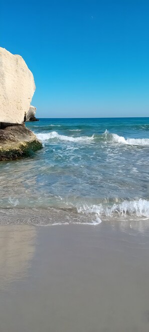 Une plage avec une eau cristalline, des vagues et une grande formation rocheuse blanche.