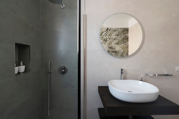 Une salle de bain moderne avec une douche, un miroir rond et un lavabo blanc.
