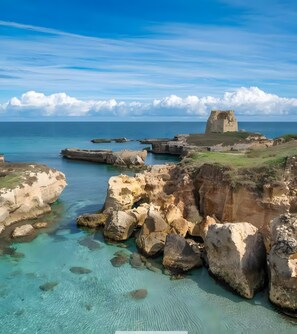 Un paysage côtier caractérisé par des formations rocheuses, des eaux turquoise cristallines et une structure en pierre d’époque.